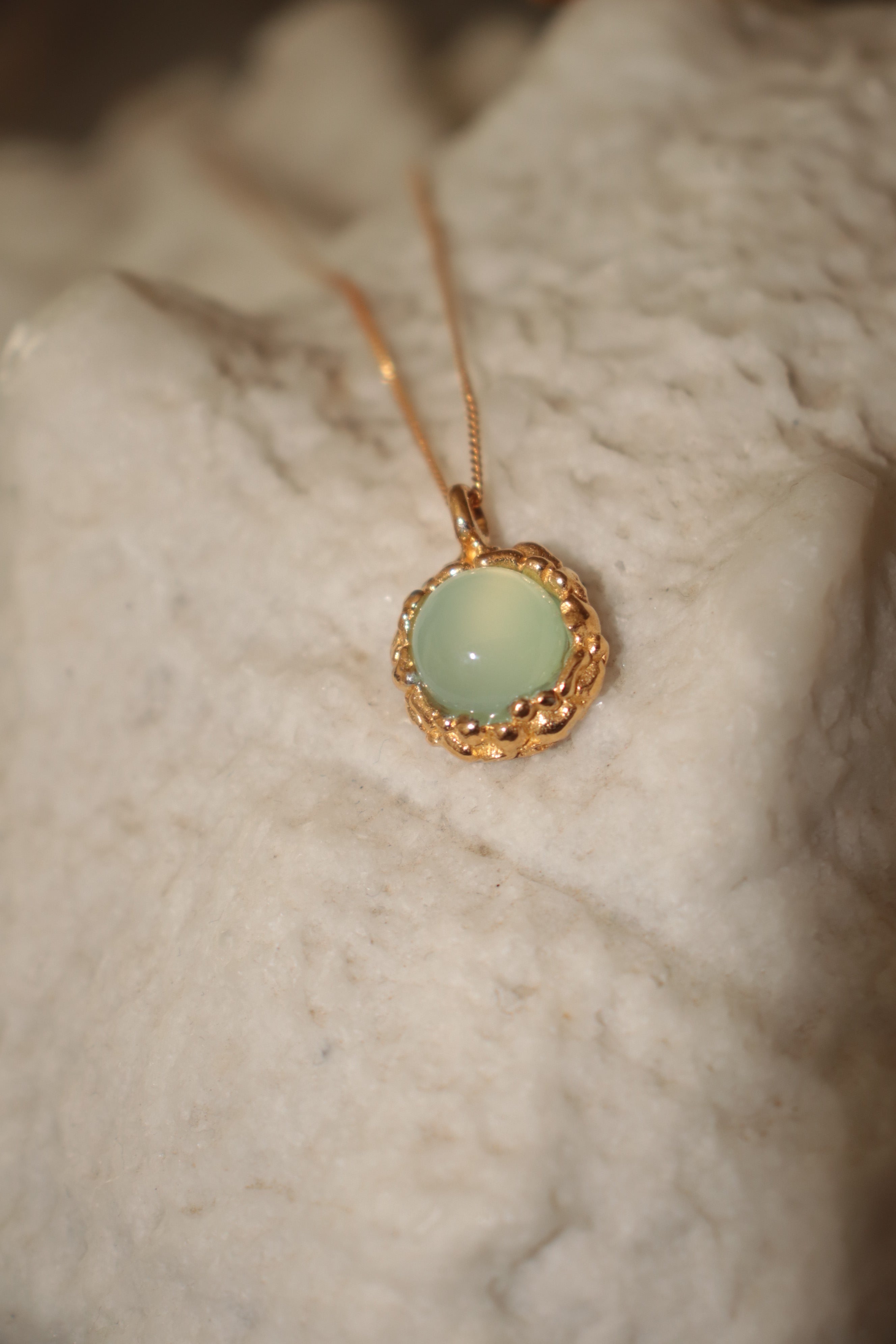 Atrani Studio Gold necklace with a light green pendant on a textured surface