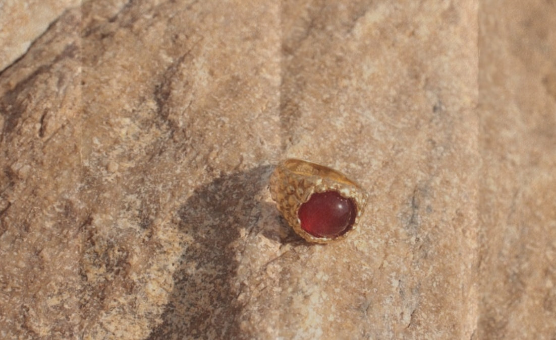 Red stone embedded in a brown rock surface atrani studio ring We use natural cabochon stones sourced responsibly, alongside 925 sterling silver, recycled brass, and 18k to 24k gold plating. Every finish is done with care, and every material is chosen for its balance between quality, durability, and minimal environmental impact.